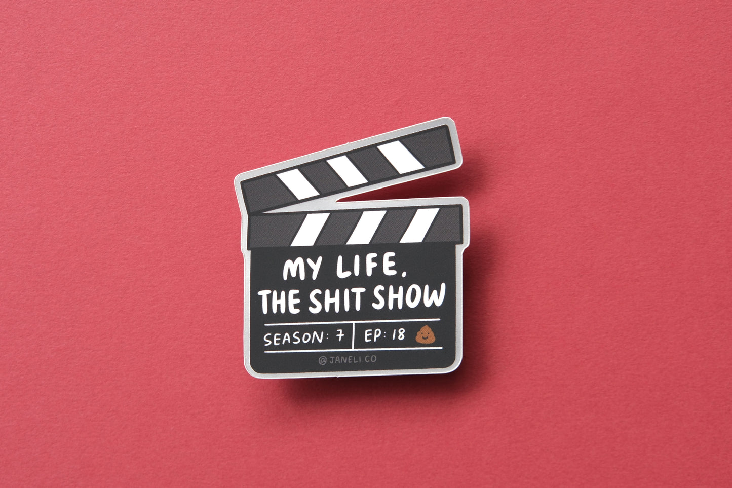 A JaneLi.Co sticker of a movie clapper that says "My life, the shit show" over a maroon background.