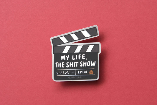 A JaneLi.Co sticker of a movie clapper that says "My life, the shit show" over a maroon background.