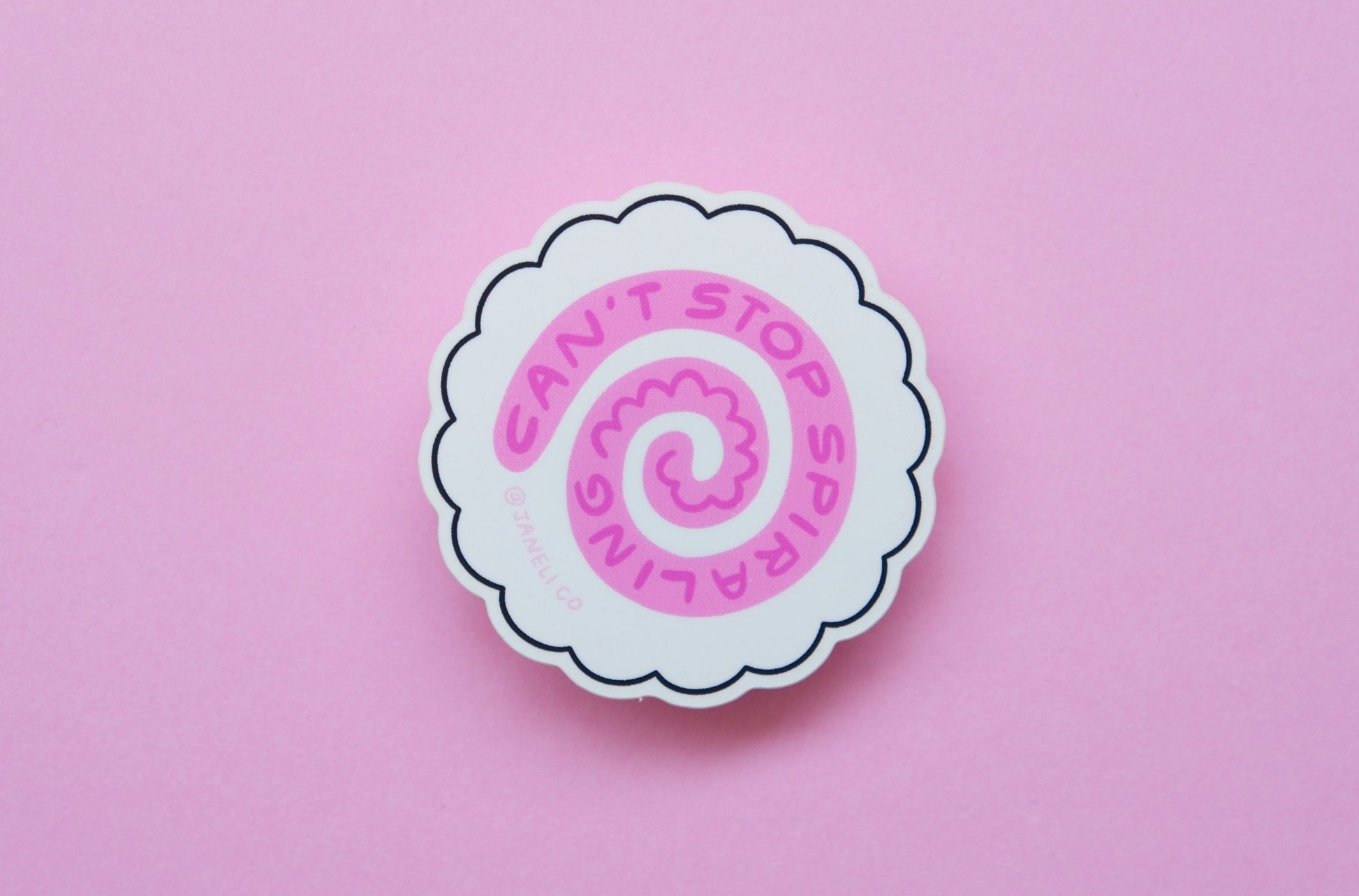 A JaneLi.Co sticker of a white fish cake with a pink swirl that says "Can't stop spiraling" over a pink background.