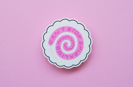 A JaneLi.Co sticker of a white fish cake with a pink swirl that says "Can't stop spiraling" over a pink background.