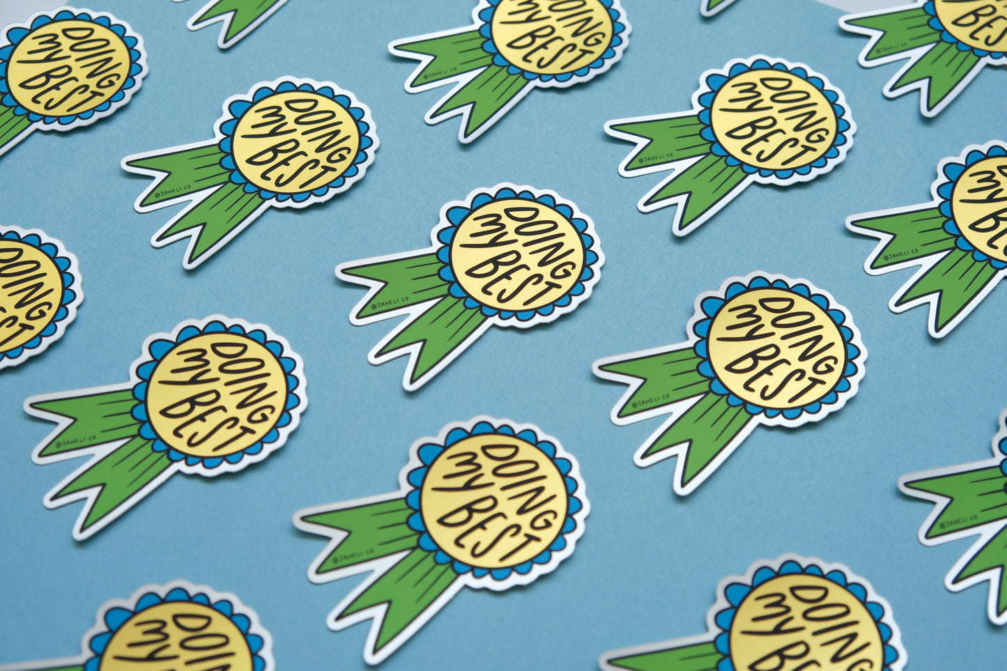 A grid of JaneLi.Co stickers of blue and green award ribbons that say "Doing My Best" over a blue background.