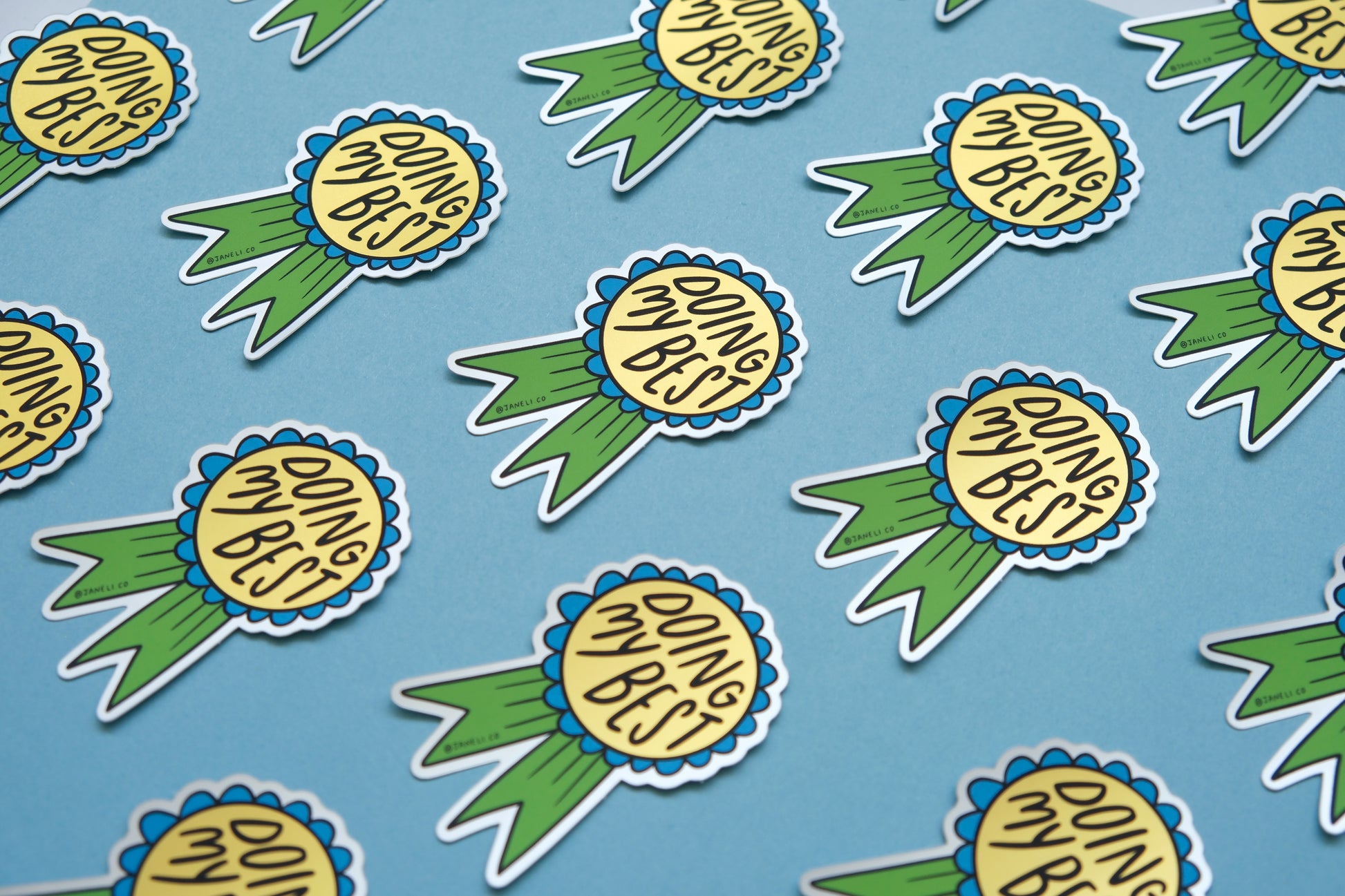 A grid of JaneLi.Co stickers of blue and green award ribbons that say "Doing My Best" over a blue background.