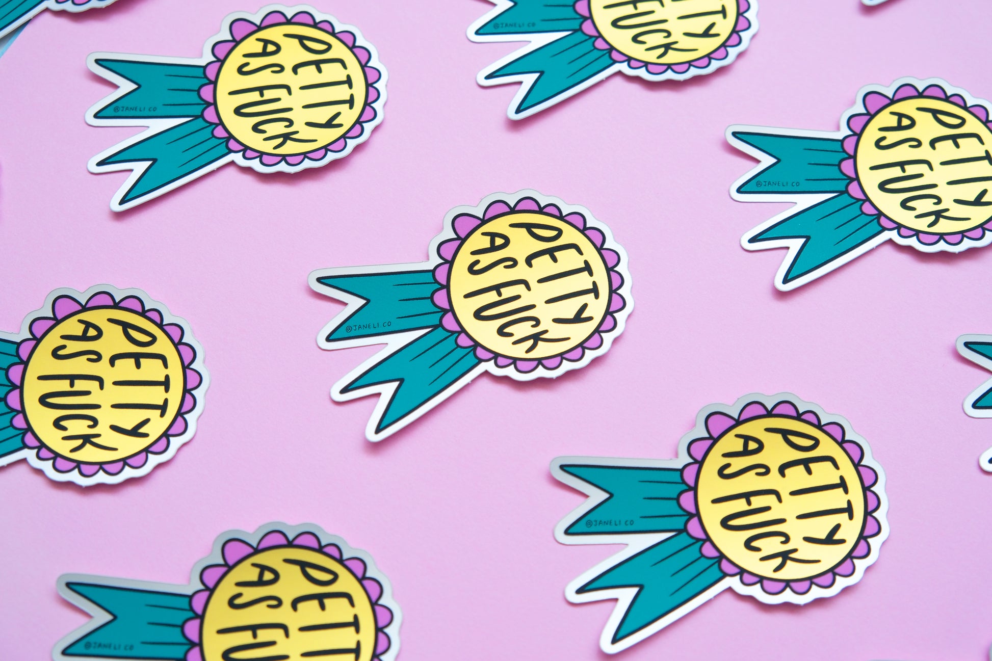A grid of JaneLi.Co stickers of pink and teal award ribbons that say "Petty As Fuck" over a pink background.