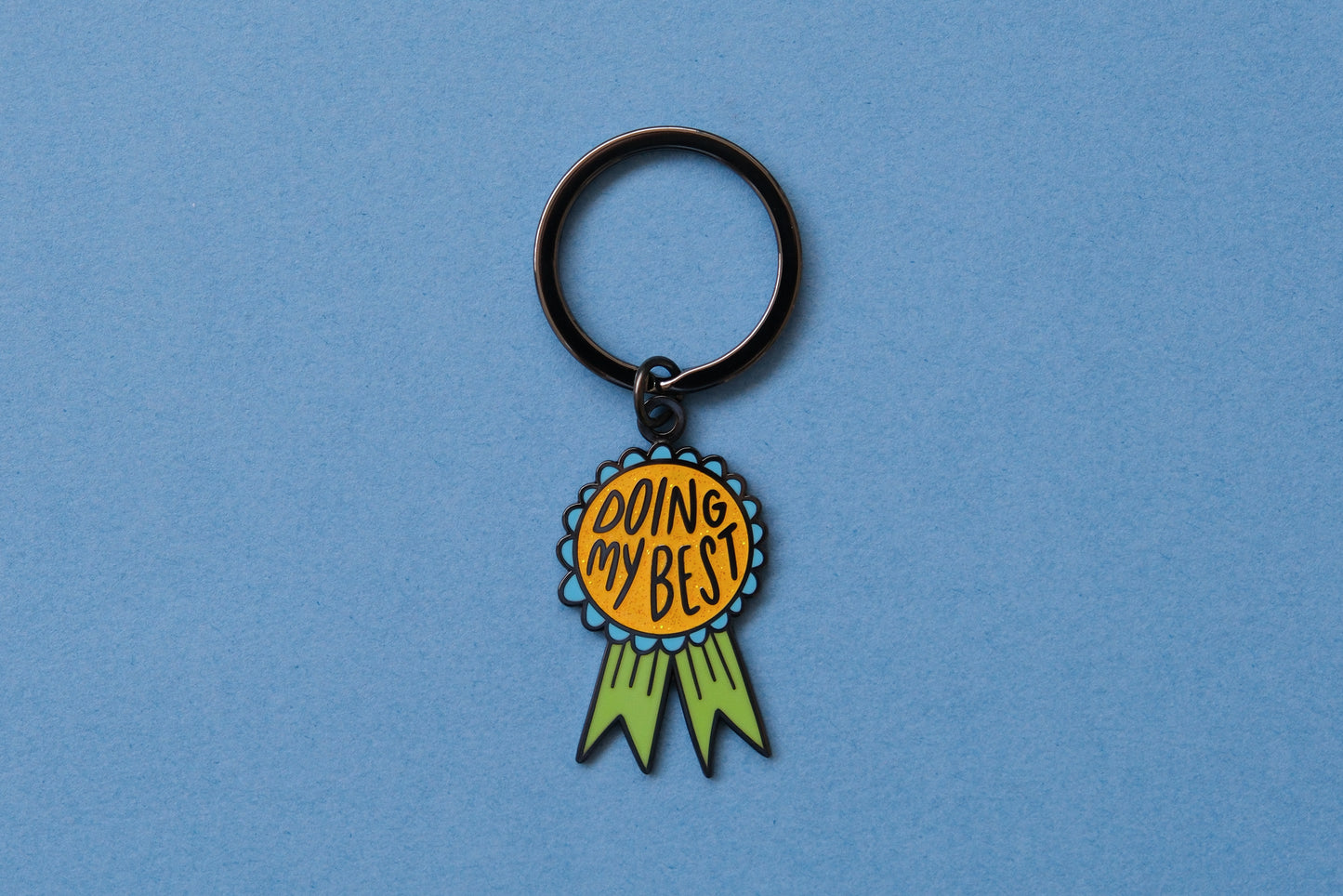 An enamel keychain showing an award ribbon that says "Doing My Best" over a blue background.