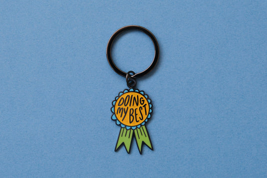 An enamel keychain showing an award ribbon that says "Doing My Best" over a blue background.
