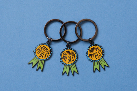 3 enamel keychains showing award ribbons that says "Doing My Best" over a blue background.