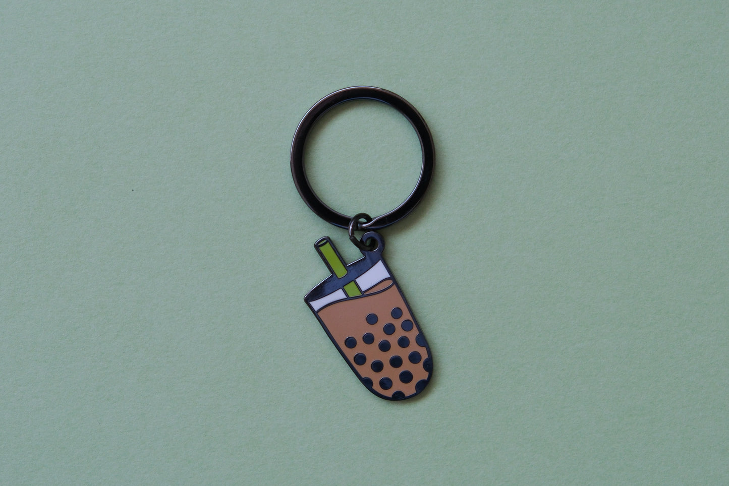 An enamel keychain showing a cup of boba with a green straw over a green background.