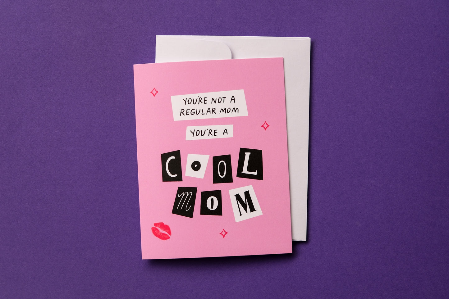 A photo of a greeting card with scrapbook cutout letters that say "You're not a regular mom you're a cool mom" and a white envelope on a purple background.
