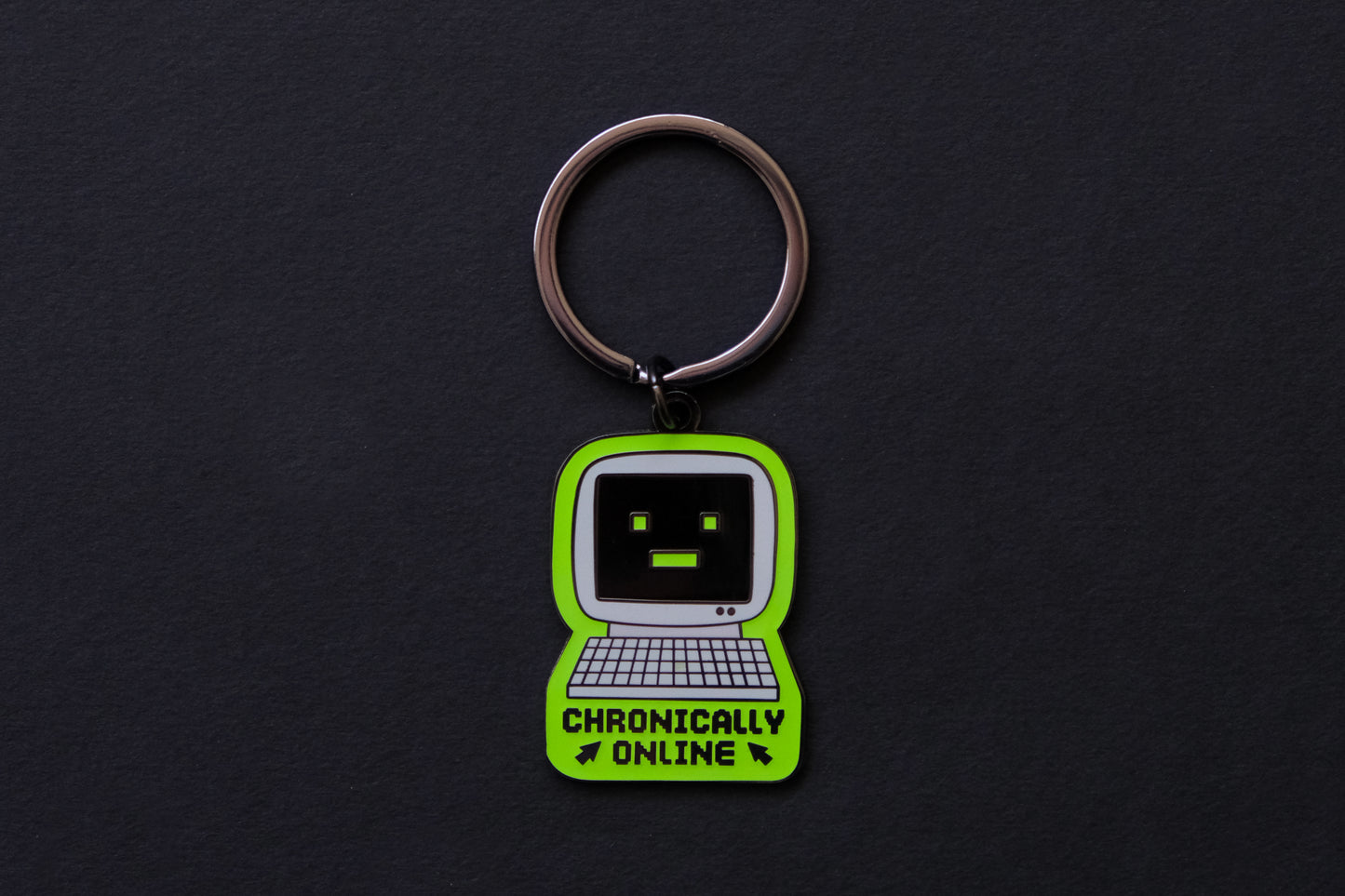 An enamel keychain of a retro computer that says "Chronically Online" over a black background.