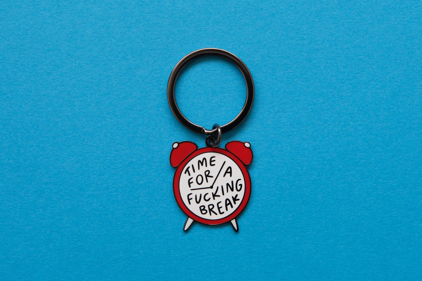 An enamel keychain of an alarm clock that says "Time for a Fucking Break" over a blue background.