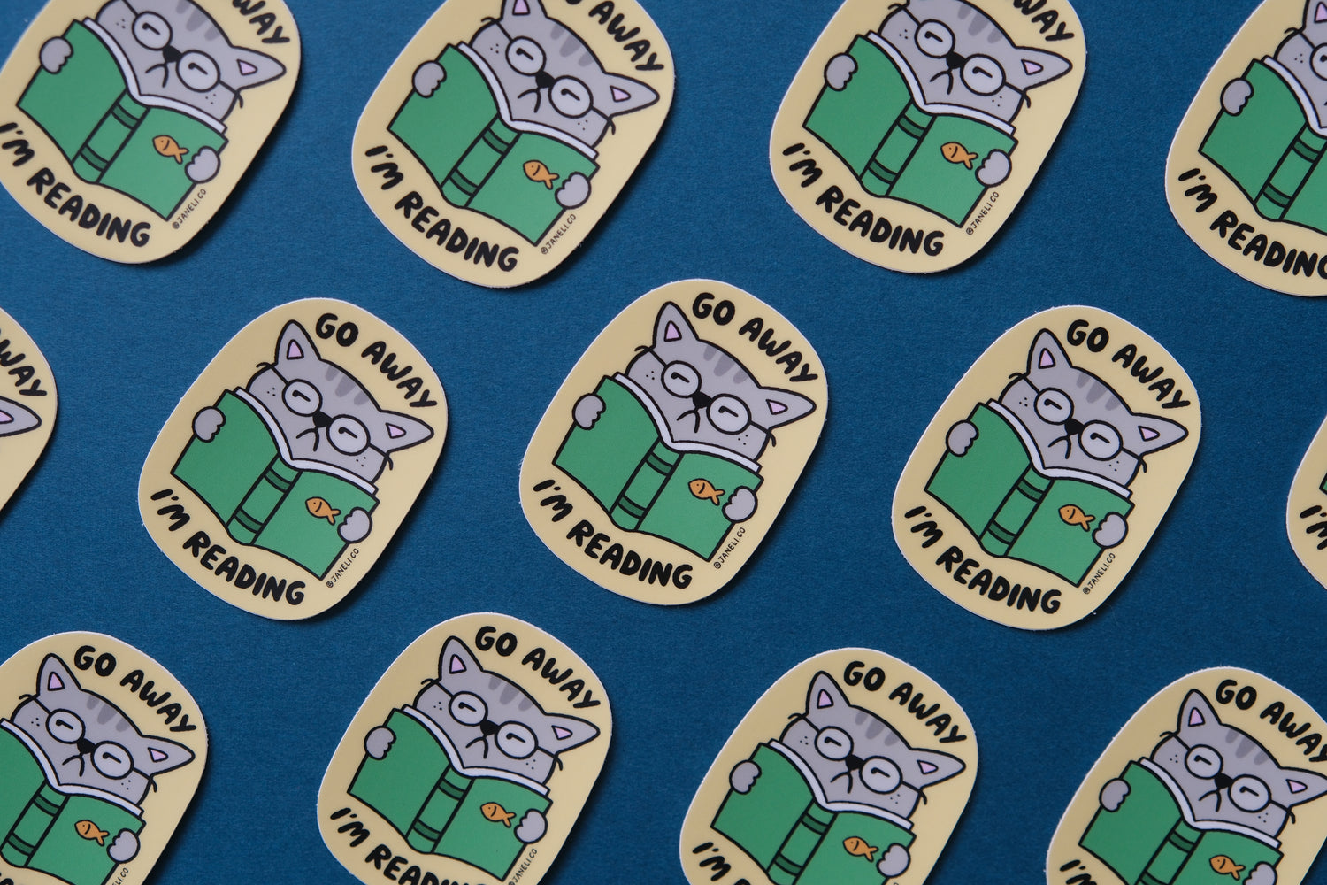 A grid of JaneLi.Co stickers of cats reading books that say "Go Away I'm Reading" over a teal background.
