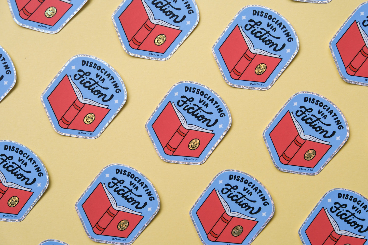 A grid of JaneLi.Co stickers of badges with books that say "Dissociating via Fiction" over a yellow background.