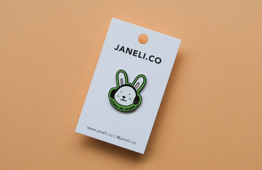 An enamel pin of a rabbit wearing headphones that says "Leave me alone" over an orange background.