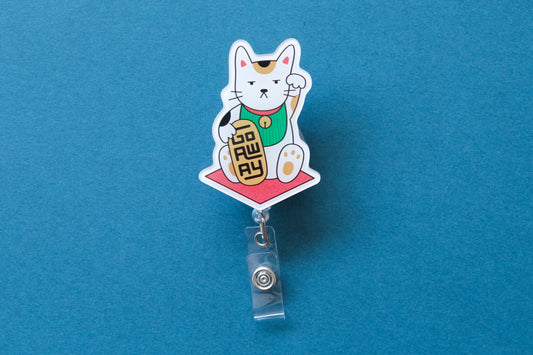 Photo of an acrylic badge reel shaped like a beckoning cat that says "Go Away" over a teal background.