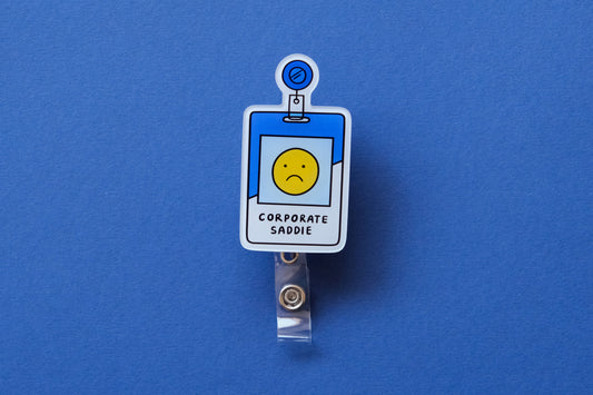 Photo of an acrylic badge reel shaped like a corporate badge that says "Corporate Saddie" over a dark blue background.