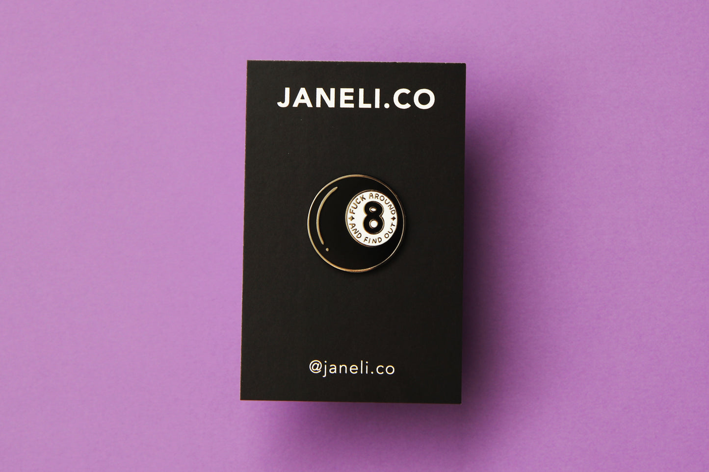 An enamel pin showing a magic 8 ball that says "Fuck around and find out" on a black JaneLi.Co backing card over a purple background.