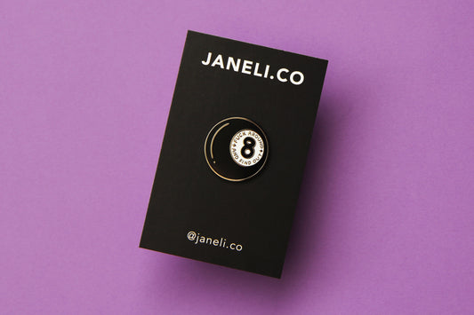 An enamel pin showing a magic 8 ball that says "Fuck around and find out" on a black JaneLi.Co backing card over a purple background.