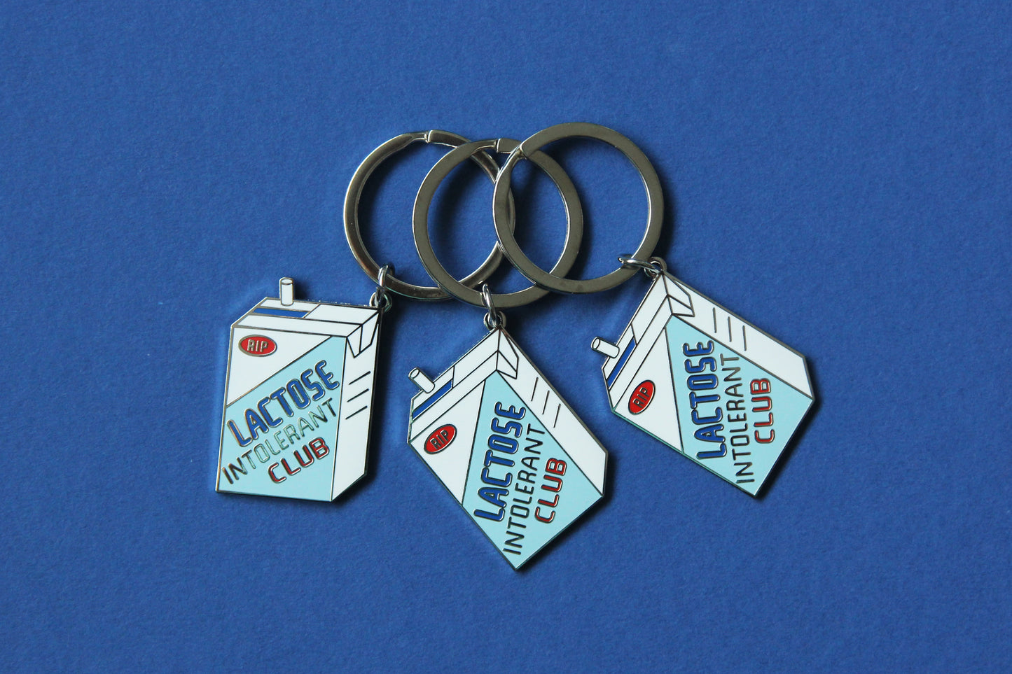 3 enamel keychains showing a soymilk carton that says" Lactose Intolerant Club" over a blue background.