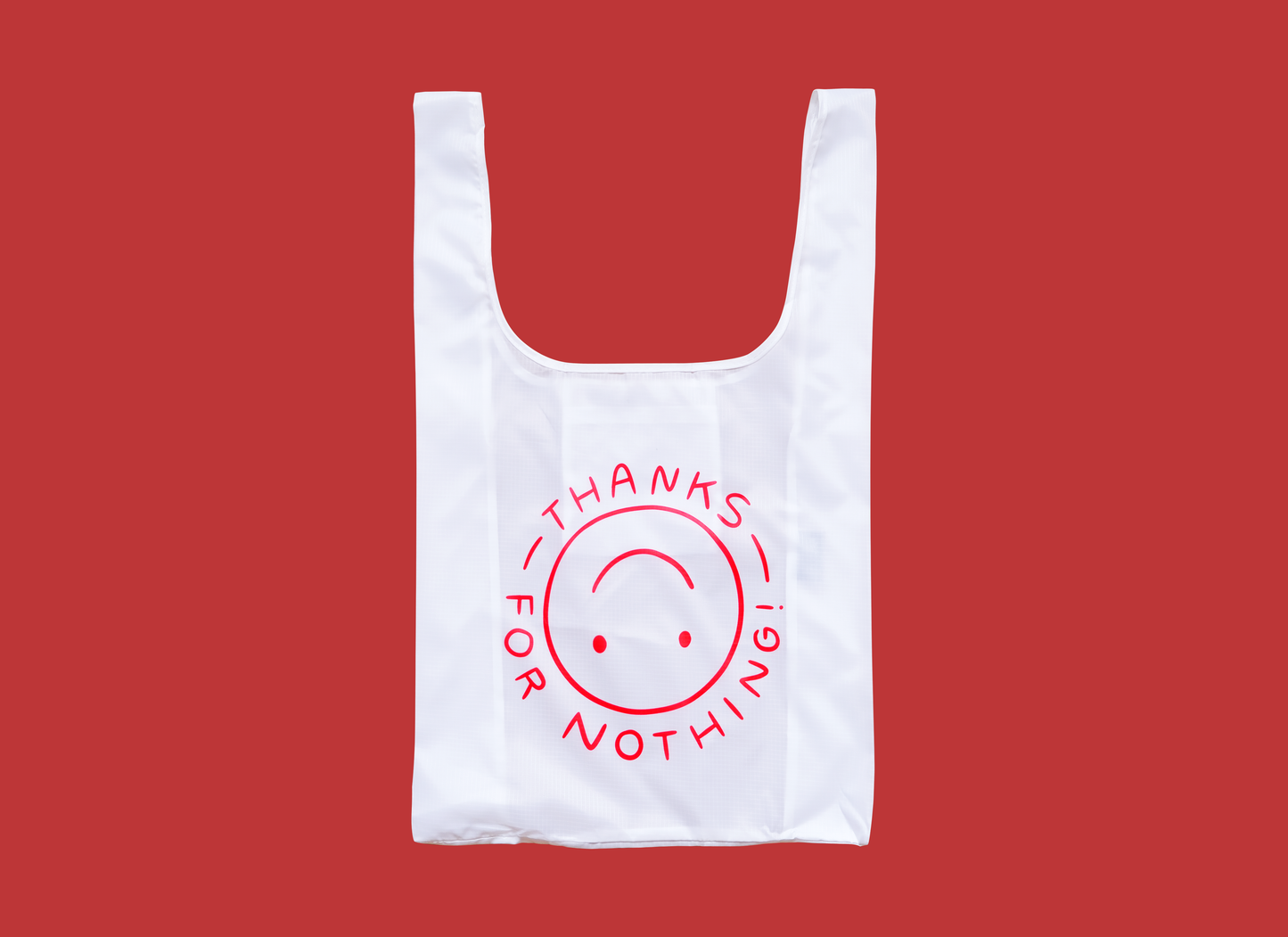 A photo of a white foldable grocery bag with an upside down smiley face that says "Thanks for nothing" over a red background.