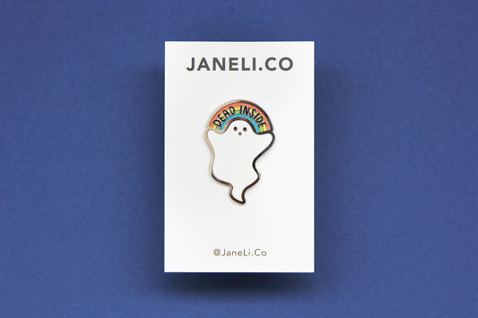 An enamel pin showing a little white ghost holding a rainbow that says "Dead Inside" on a white JaneLi.Co backing card over a navy background.