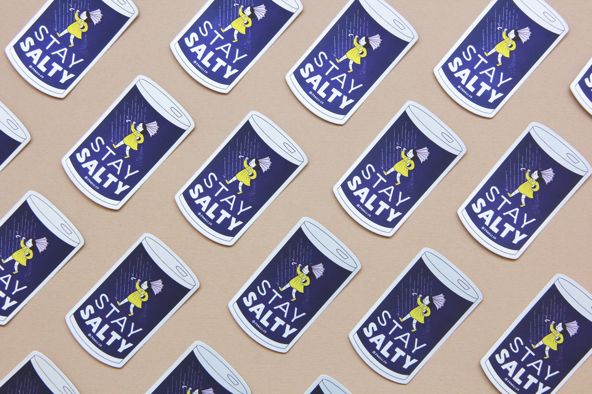 A grid of JaneLi.Co stickers that say "Stay Salty" in the shape of salt cans with angry salt girls holding umbrellas blow backwards from wind and rain over a navy blue background.