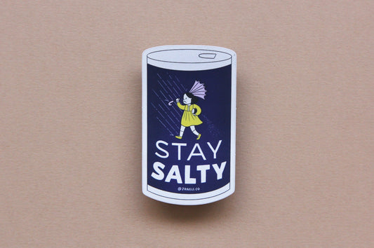 A JaneLi.Co sticker that says "Stay Salty" in the shape of a salt can with an angry salt girl holding an umbrella blow backwards from wind and rain over a navy blue background.