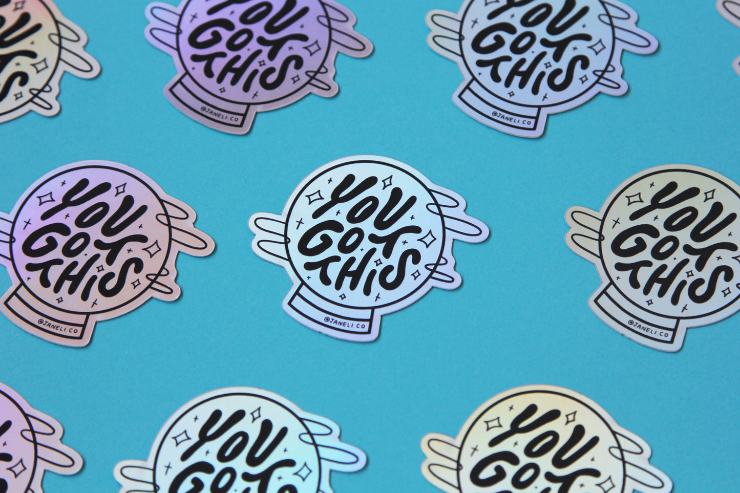 A grid of holographic JaneLi.Co stickers that say "You Got This" in a magic crystal ball over a blue background.