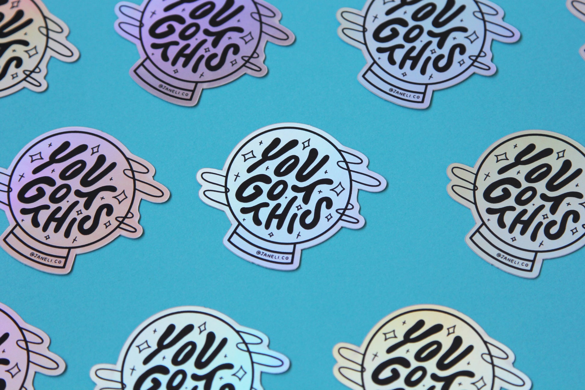 A grid of holographic JaneLi.Co stickers that say "You Got This" in a magic crystal ball over a blue background.