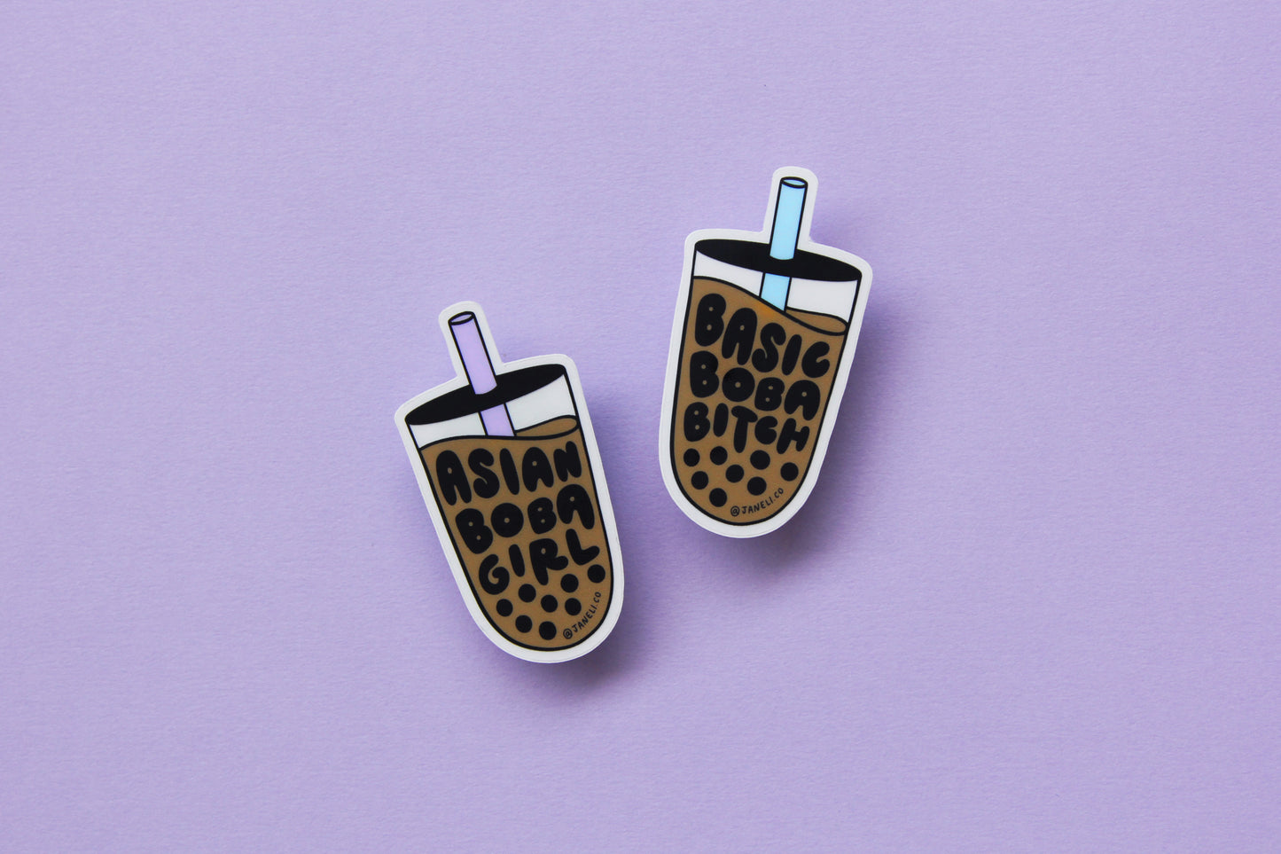 Two JaneLi.Co stickers in the shape of cups of boba over a lavender background. One of the cups says "Asian Boba Girl" with a purple straw, and the other says "Basic Boba Bitch" with a blue straw.
