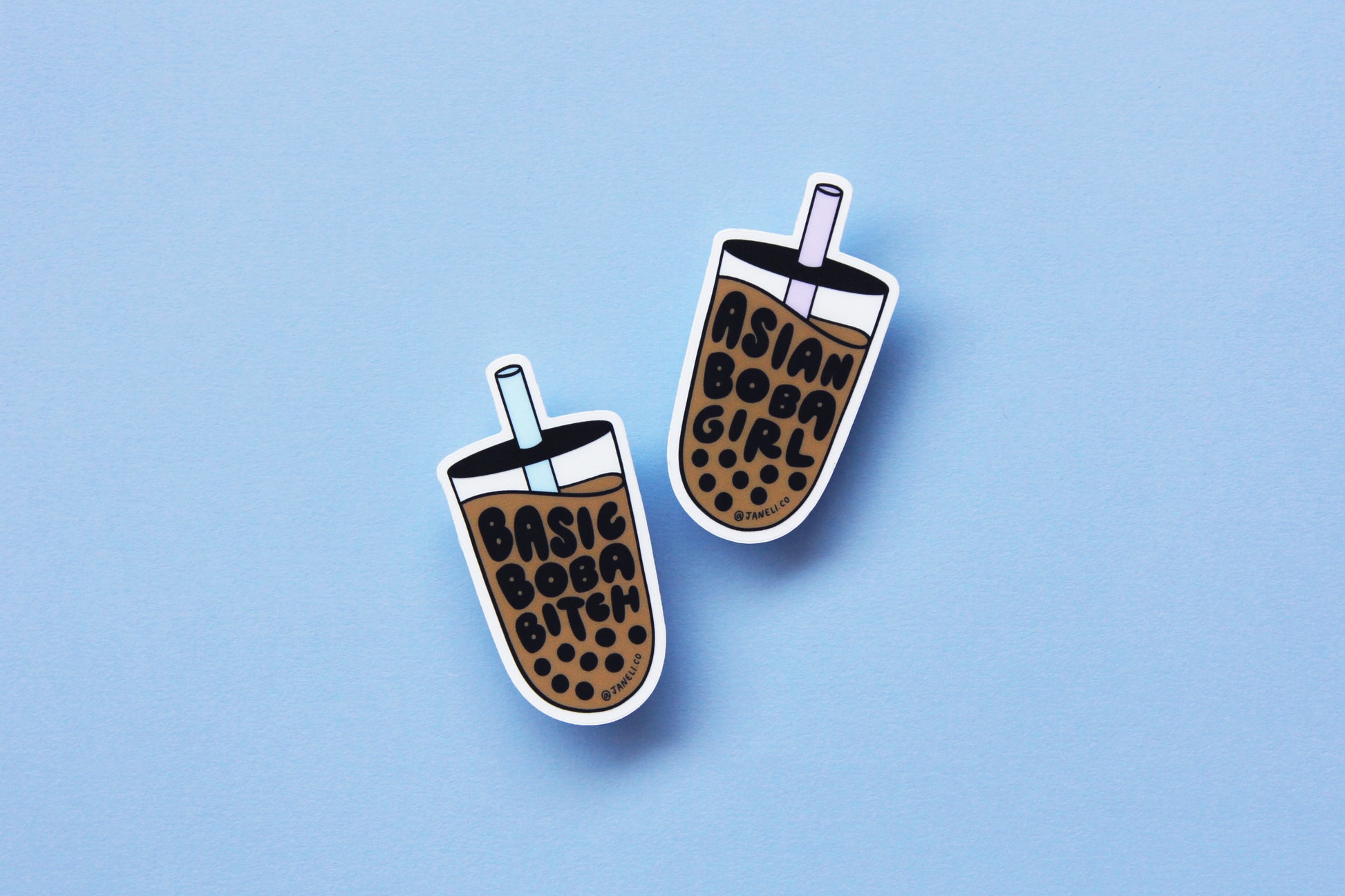 Two JaneLi.Co stickers in the shape of cups of boba over a sky blue background. One of the cups says "Basic Boba Bitch" with a blue straw, and the other says "Asian Boba Girl" with a purple straw.