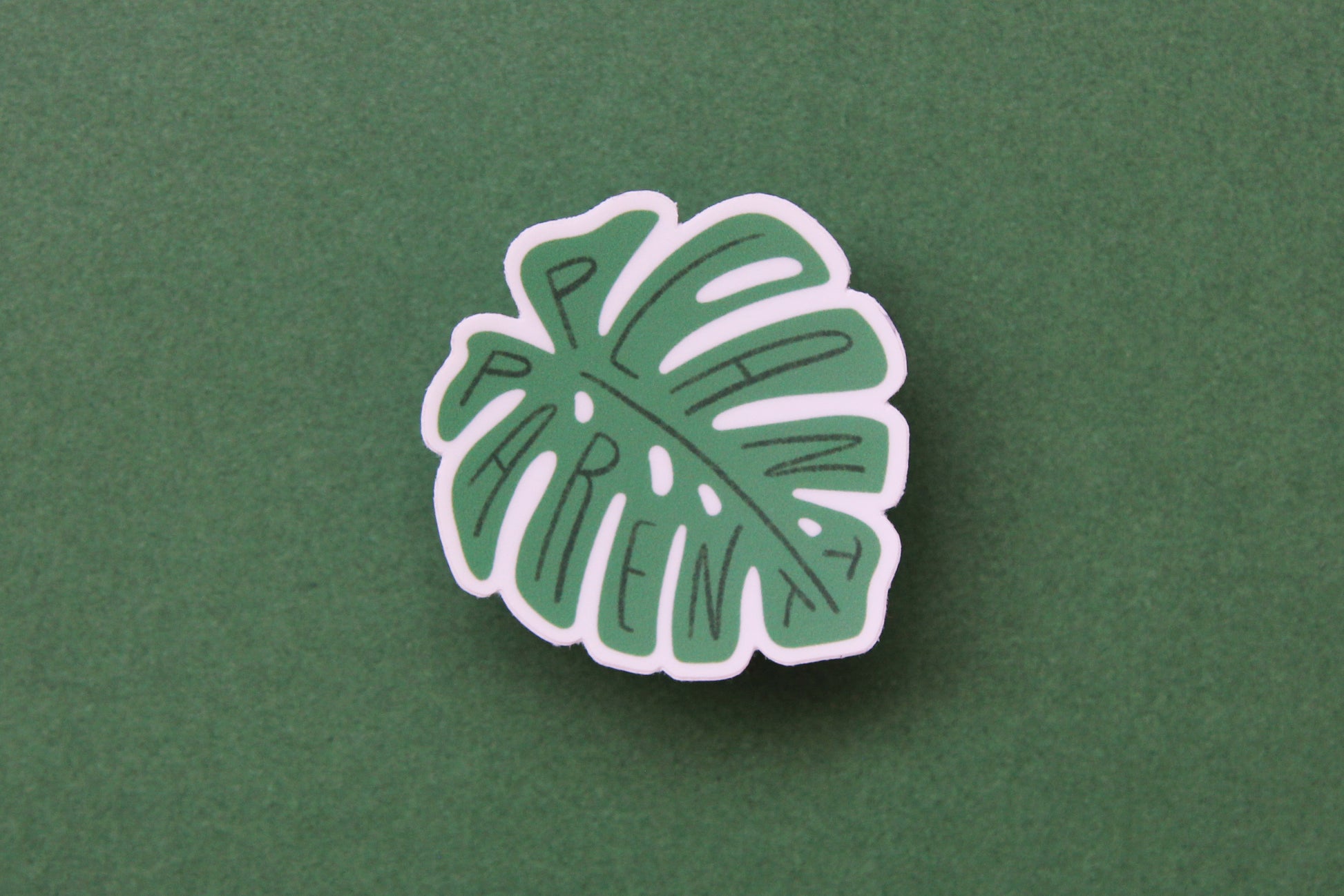 A green JaneLi.Co sticker that says "Plant Parent" in the shape of a monstera leaf over a green background.