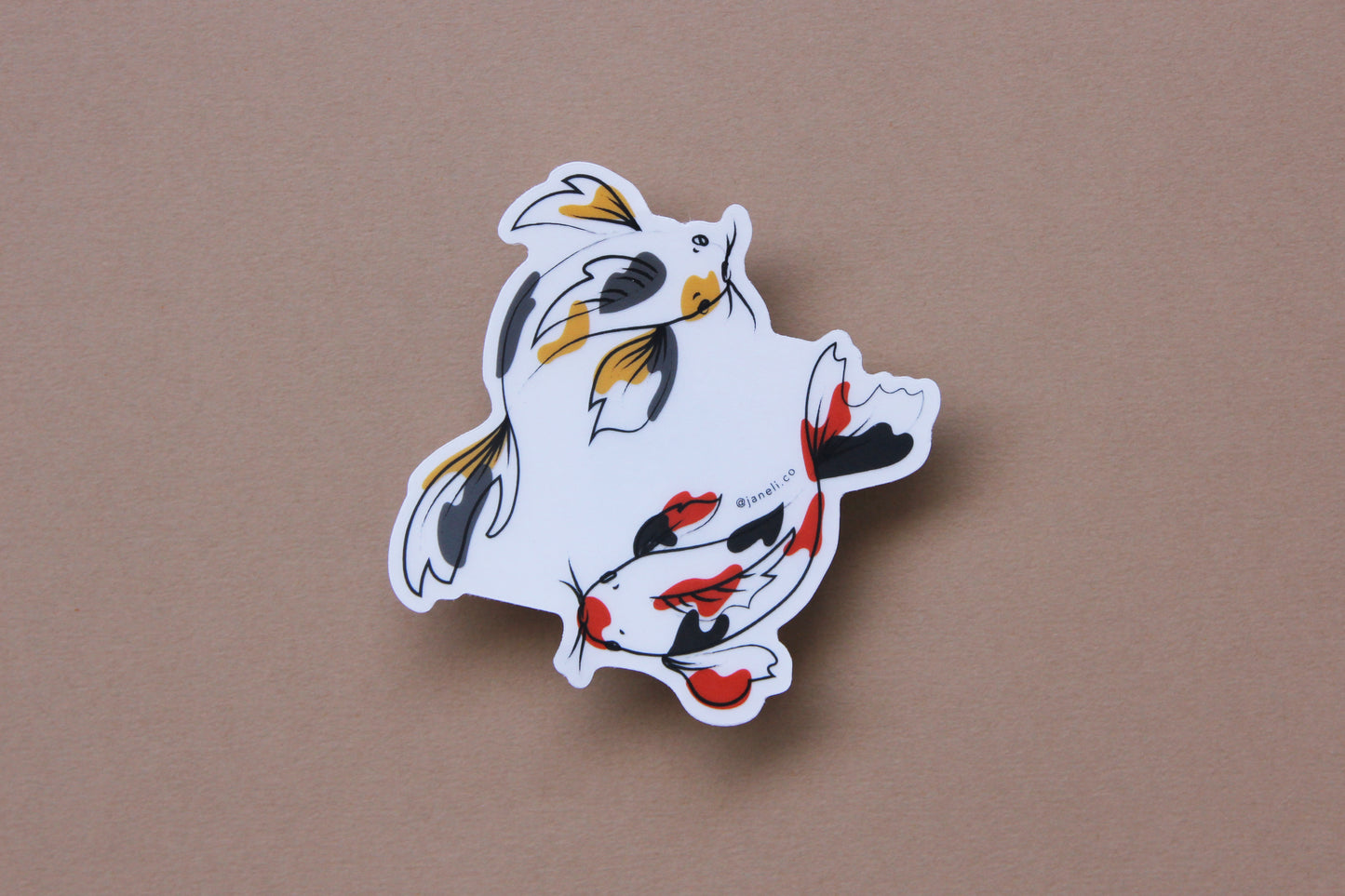 A JaneLi.Co sticker of a gold and grey koi fish and a scarlet and black koi fish swimming in a circle over a tan background.