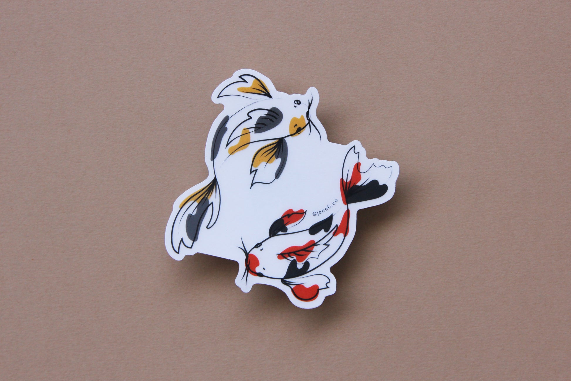 A JaneLi.Co sticker of a gold and grey koi fish and a scarlet and black koi fish swimming in a circle over a tan background.