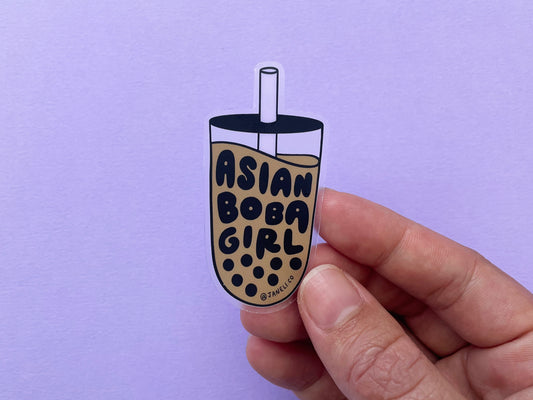 A hand holding a clear JaneLi.Co sticker that says "Asian Boba Girl" in the shape of a cup of boba over a lavender background.