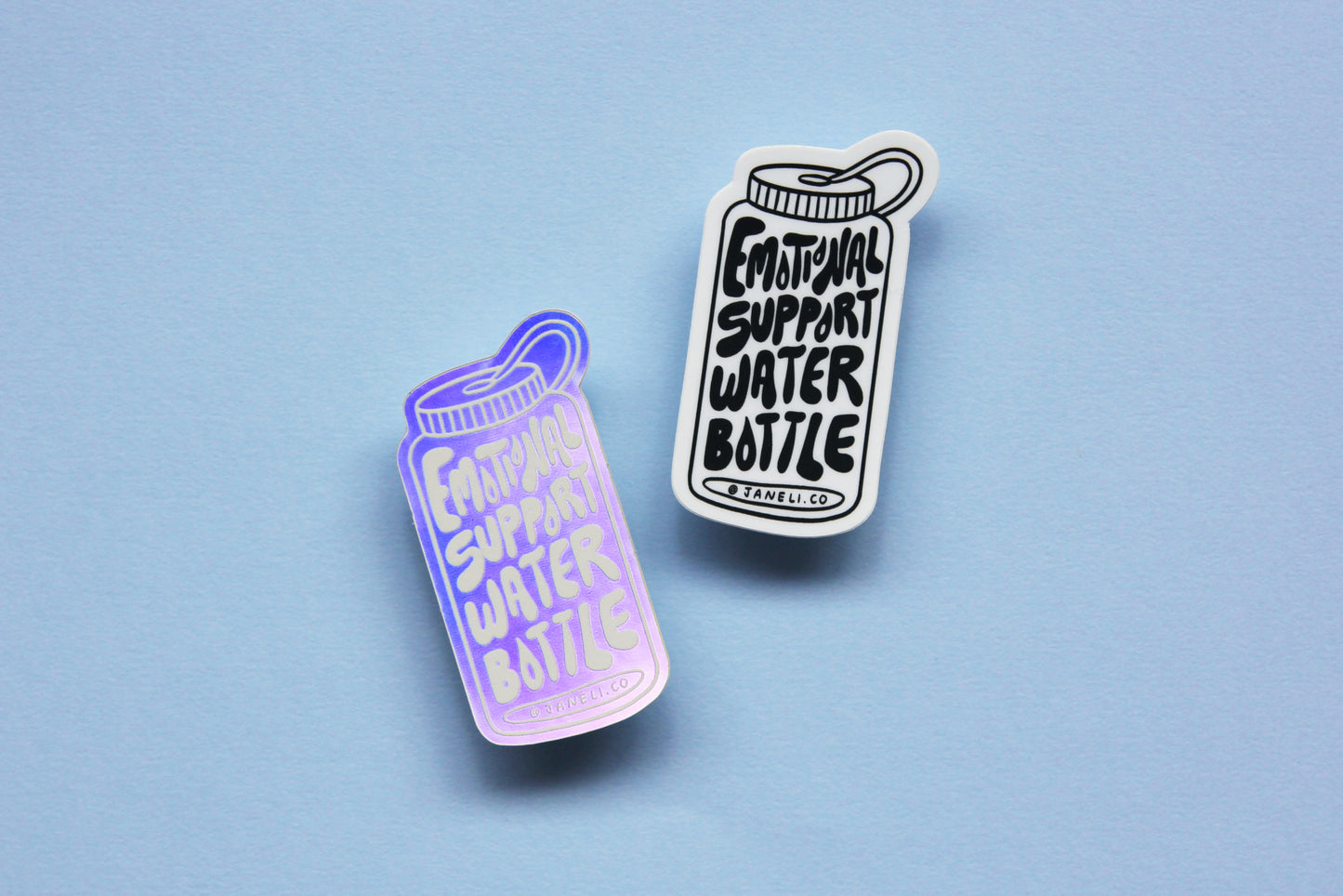 Two JaneLi.Co stickers that say "Emotional Support Water Bottle" in the shape of a water bottle over a sky blue background. One sticker is black and white, and the other is holographic.