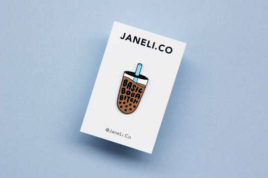 An enamel pin showing a cup of boba that says "Basic Boba Bitch" with a blue straw on a white JaneLi.Co backing card over a blue background.