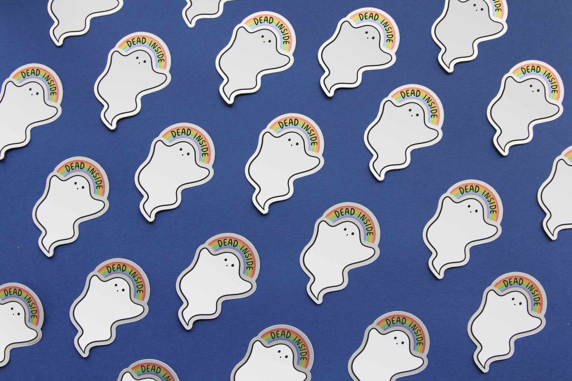 A grid JaneLi.Co stickers that show little white ghosts holding up rainbows that says "Dead Inside" over a navy blue background. Each sticker has a metallic silver border.