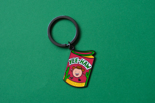 An enamel keychain showing a roll of haw flakes that says "Yee-Haw" over a green background.