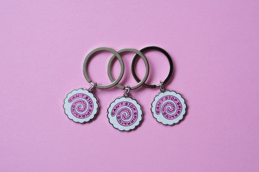 3 enamel keychains showing narutomaki fishcakes that say "Can't Stop Spiraling" over a pink background.