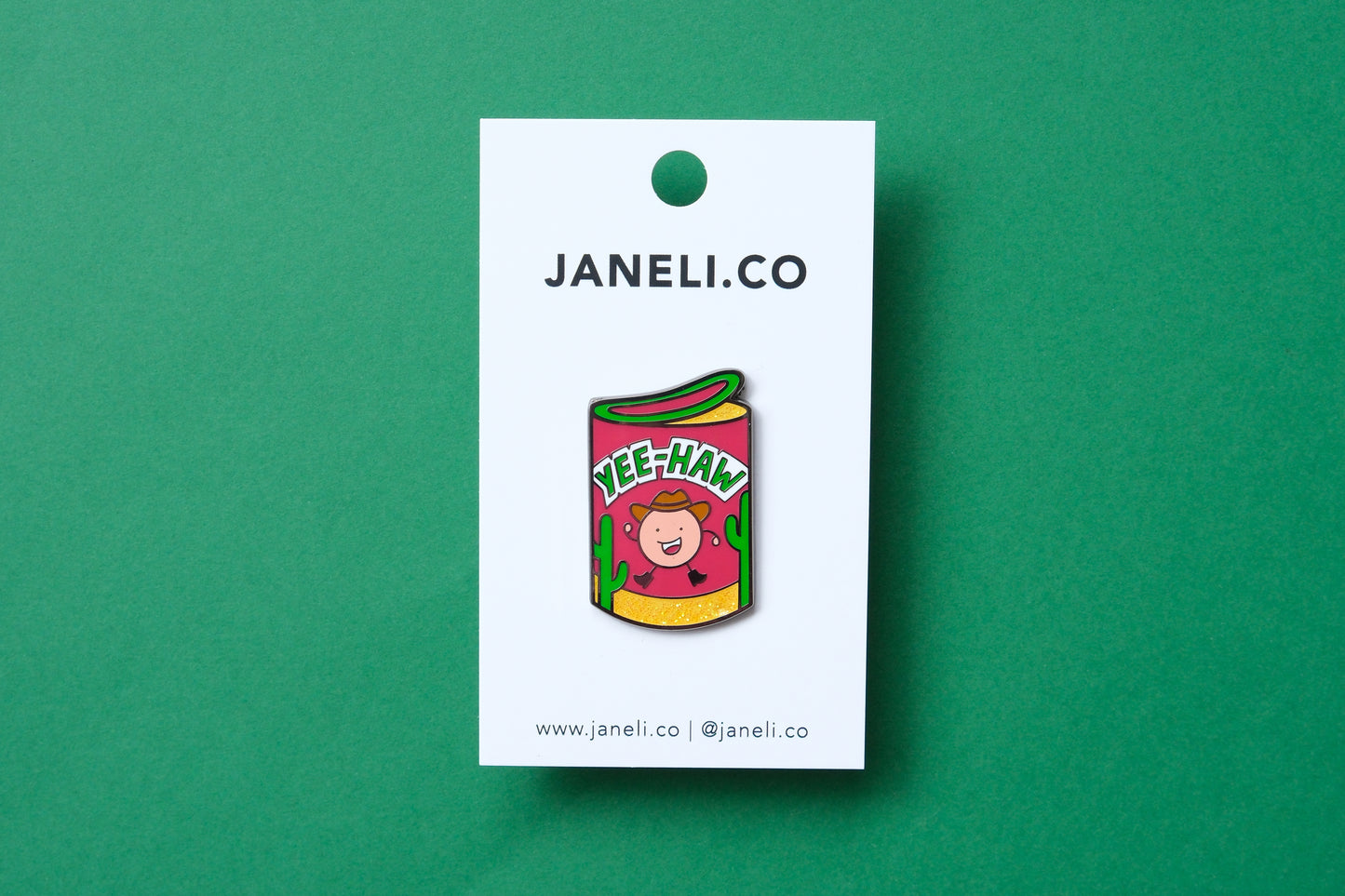 An enamel pin showing a roll of haw flakes that says "Yee-Haw" on a white JaneLi.Co backing card over a green background.