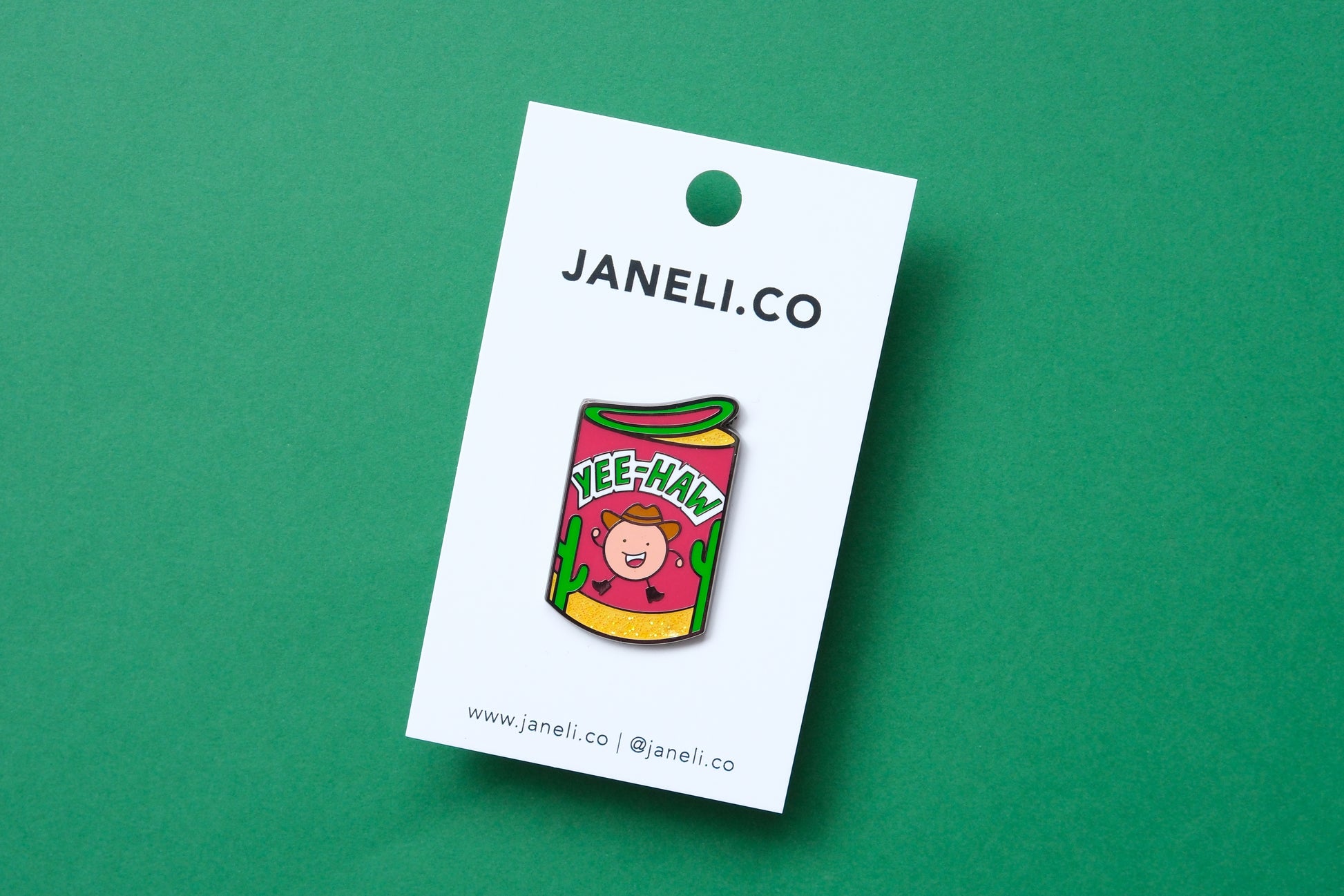 An enamel pin showing a roll of haw flakes that says "Yee-Haw" on a white JaneLi.Co backing card over a green background.