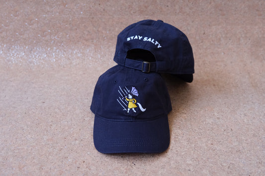 A photo of a navy dad hat with an embroidered grumpy salt girl and the back of a second navy dad hat with "Stay Salty" embroidered on the back in white.