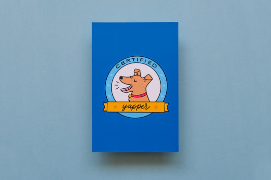 A JaneLi.Co mini print/postcard of a badge with a barking dog that says "Certified Yapper" over a blue background.