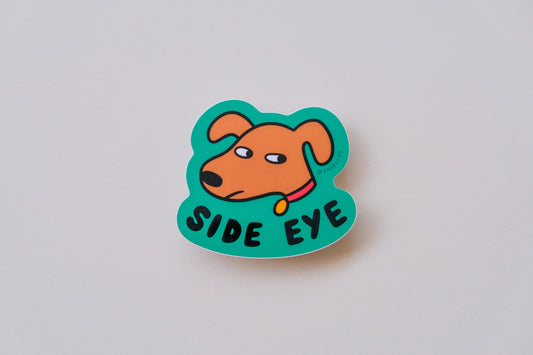 A JaneLi.Co sticker of a dog giving side eye that says "Side Eye" over a cream background.