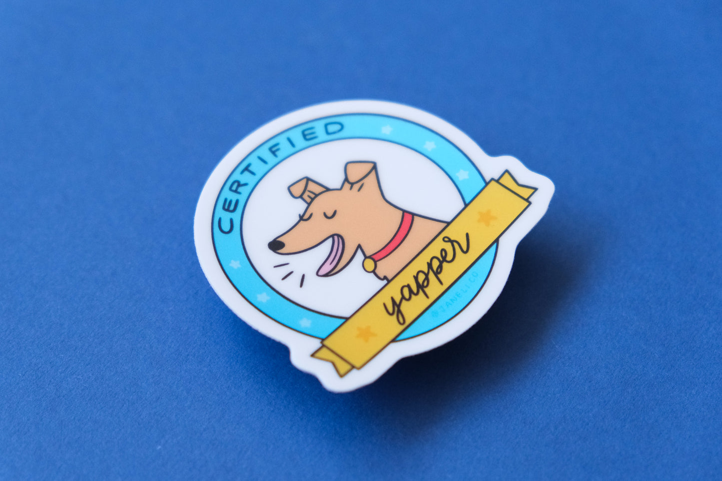 A JaneLi.Co sticker of a badge with a barking dog that says "Certified Yapper" over a blue background.