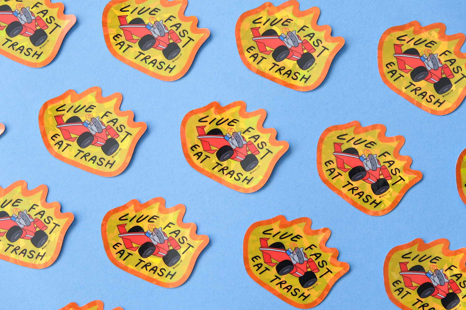 A grid of JaneLi.Co stickers of raccoons driving racecars with flames while slurping sodas that say "Live Fast Eat Trash" over a blue background.