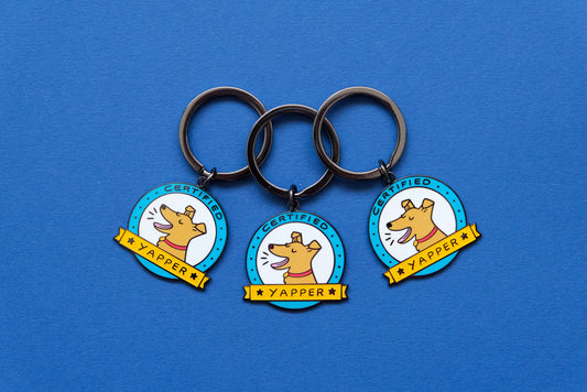 3 enamel keychains showing barking dogs that say "Certified Yapper" over a blue background.