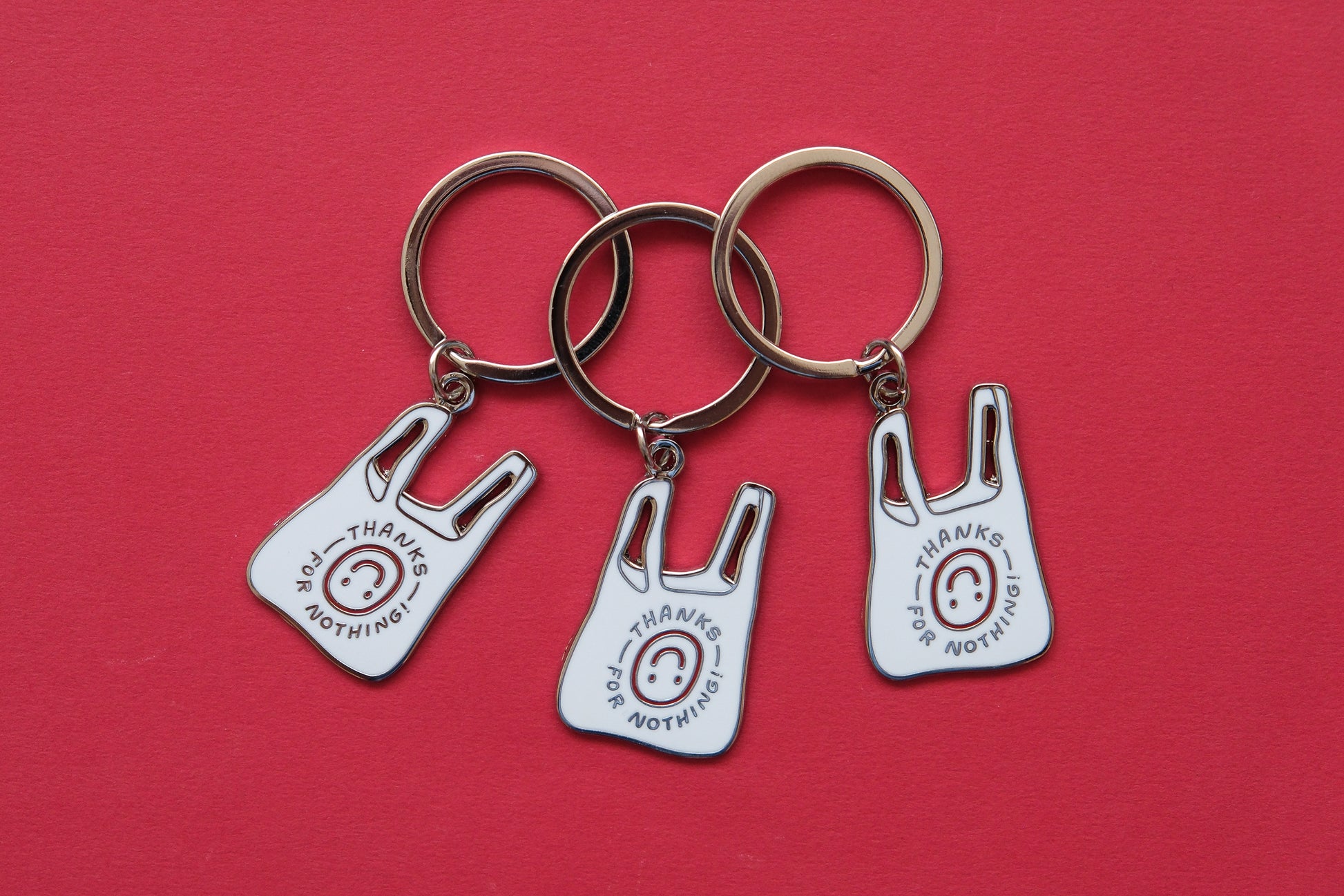 3 enamel keychains showing plastic takeout bags that says "Thanks for nothing" with an upside down smiley face over a red background.