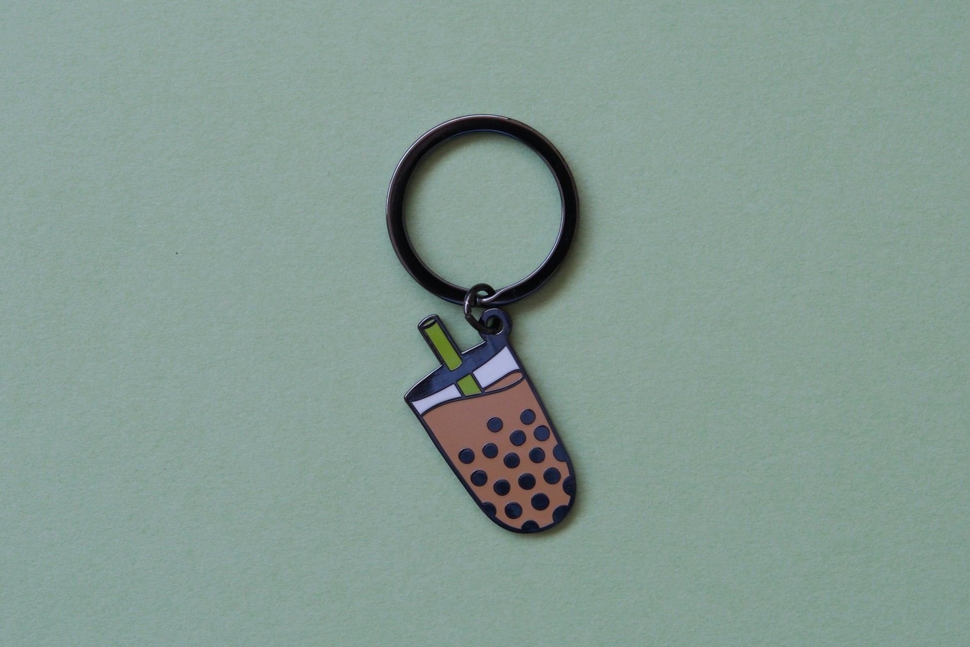 An enamel keychain showing a cup of boba with a  green straw over a green background.