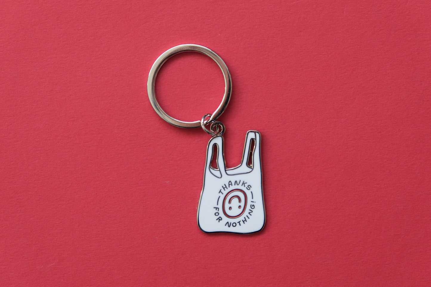 An enamel keychain showing a plastic takeout bag that says "Thanks for nothing" with an upside down smiley face over a red background.